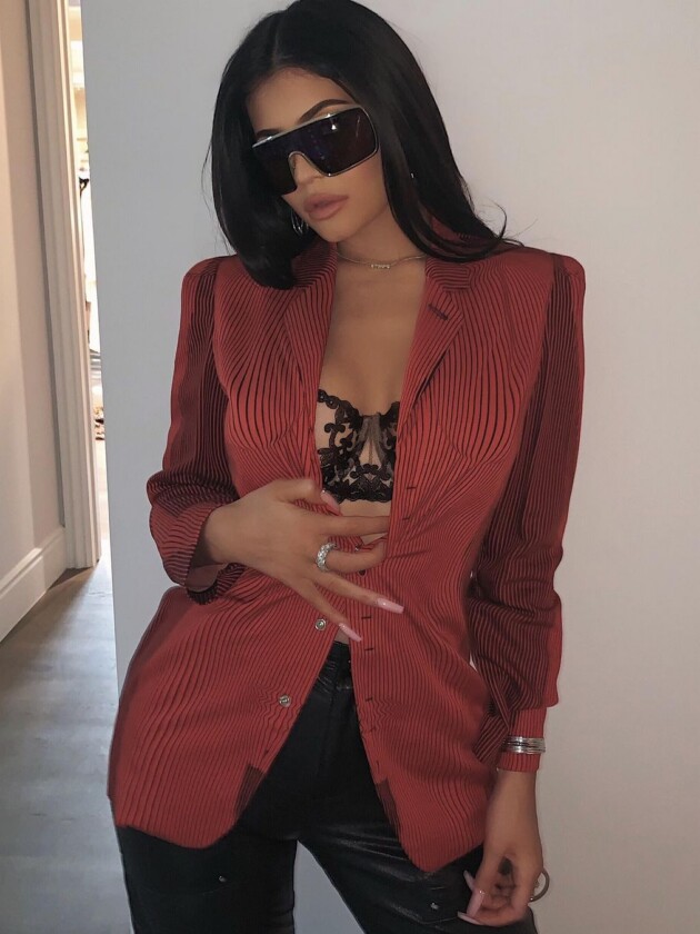 A evolução do estilo de Kylie Jenner Kylie Jenner usa blazer vermelho de listras com sutiã rendado preto por baixo