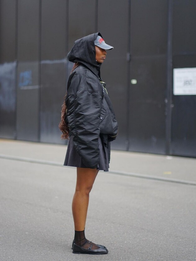 Sapatilha no look esportivo. | Foto: Instagram/@by.regiina sapatilha com tira é usada com jaqueta bomber e boné em look todo preto