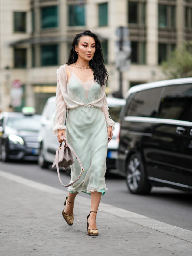 7 ideias para atualizar o slip dress neste inverno Camadas: Slip dress verde claro e acetinado é usado com blusa transparente por cima e sandália de salto