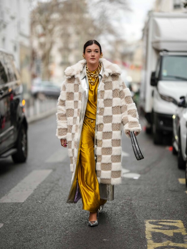 7 ideias para atualizar o slip dress neste inverno Camadas: slip dress amarelo é usado com sobreposição de casacos. O primeiro liso, e o segundo com estampa xadrez e textura de pelinhos. Cintos e colares dourados compõem o look