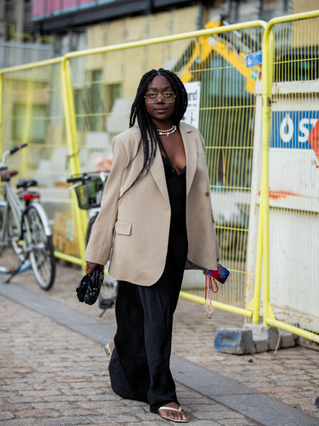 7 ideias para atualizar o slip dress neste inverno Slip dress preto é combinado com blazer bege e colar dourado