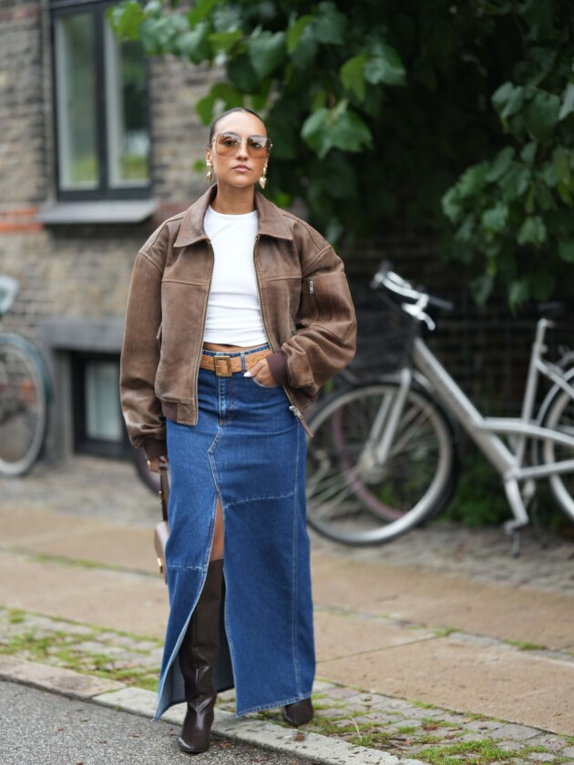 5 tendências de jeans para além do básico saia jeans comprida com fenda é usada com bota de cano alto e jaqueta de couro marrom