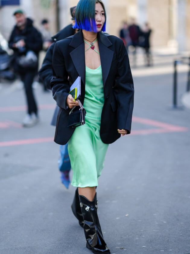 7 ideias para atualizar o slip dress neste inverno Slip dress verde é usado com alças invertidas, criando um efeito de x no colo. O look é complementado com blazer e botas pretas