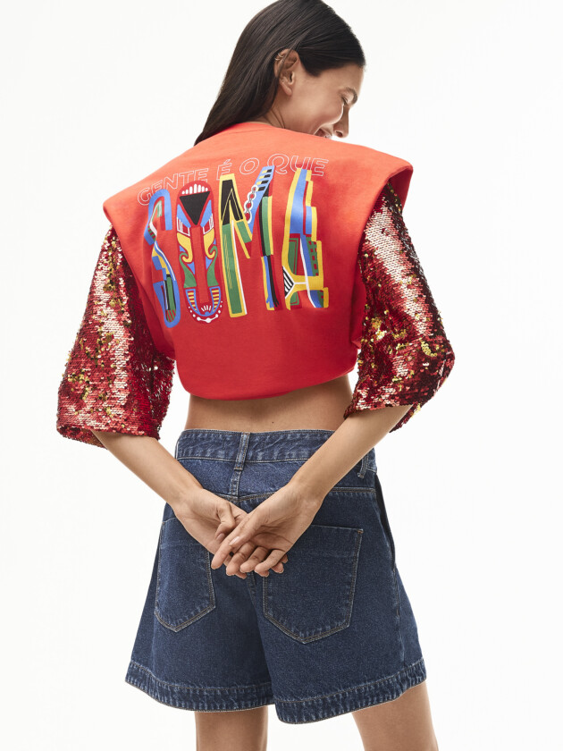 Vem ver os abadás do camarote da moda! mulher de costas, veste camiseta vermelha com mangas de paetê e a instrição Soma