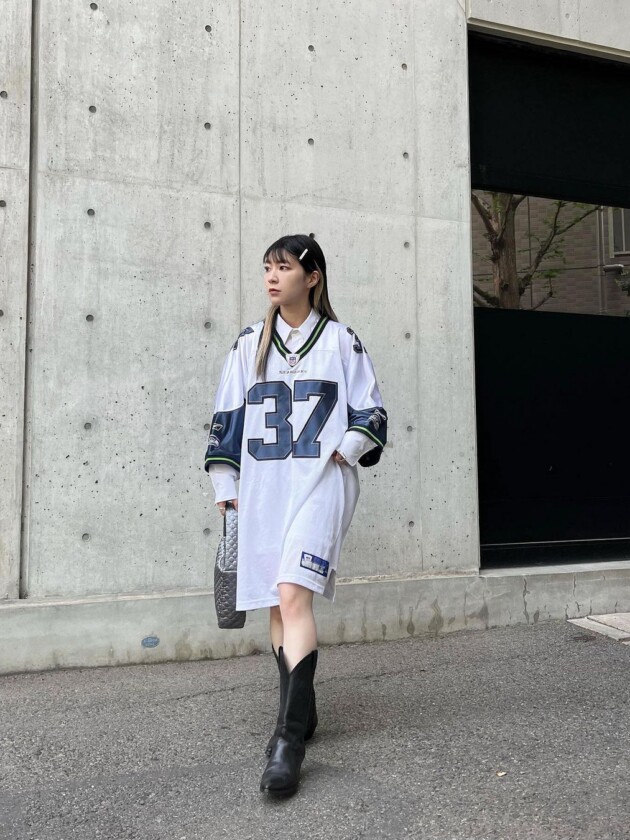 Como usar camisa de time: 5 dicas para incorporar a tendência esportiva Camisa de time esportivo oversized é usada como vestido e sobrepõe camisa social branca com gola