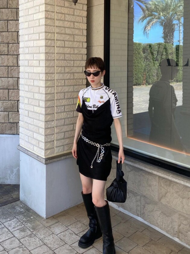 Como usar camisa de time: 5 dicas para incorporar a tendência esportiva Blusa usa camisa esportiva em baixo de vestido tomara que caia preto. Look é finalizada com bota de cano alto