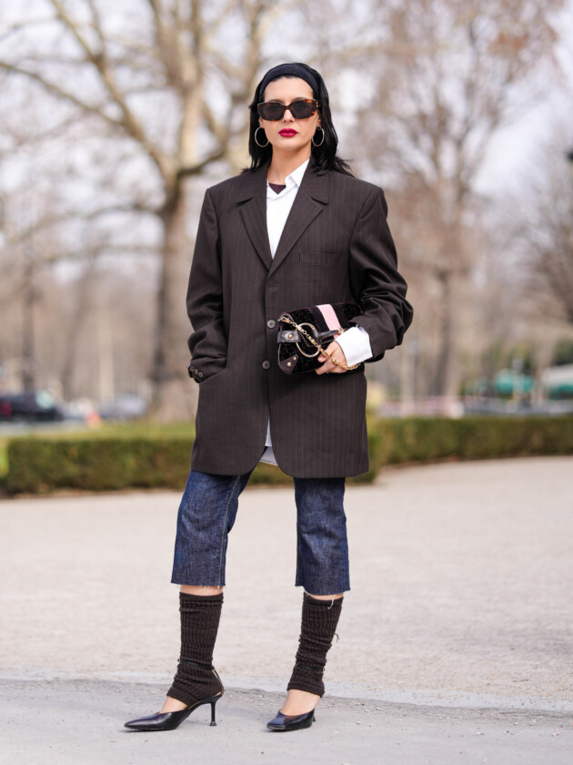 O retorno da calça capri: 5 maneiras de usar Mulher usa calça capri jeans, blazer oversized cinza, camisa branca e polaina preta em look na semana de moda de paris